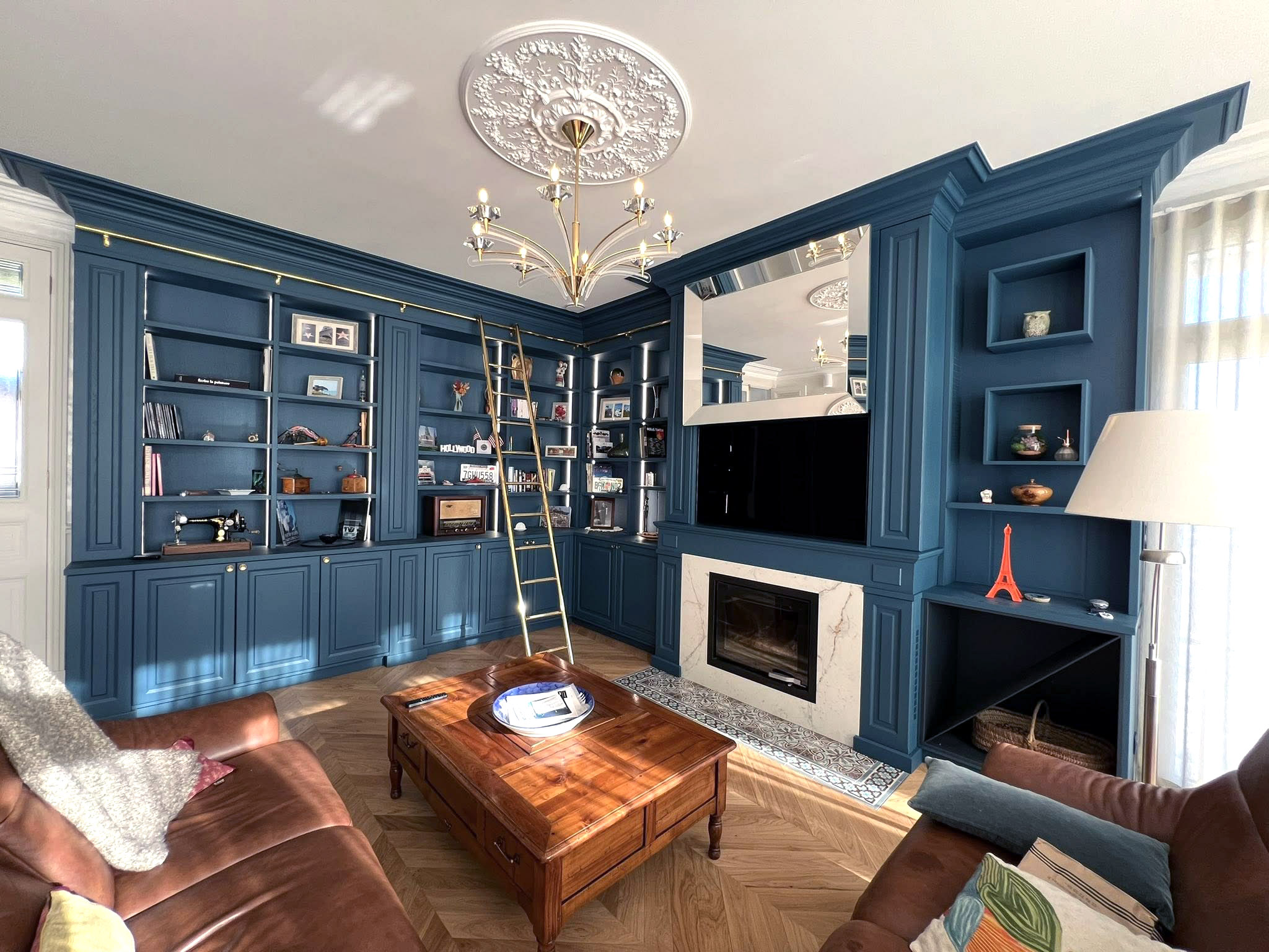 Bibliothèque murale bleue avec moulures, échelle en laiton et cheminée intégrée