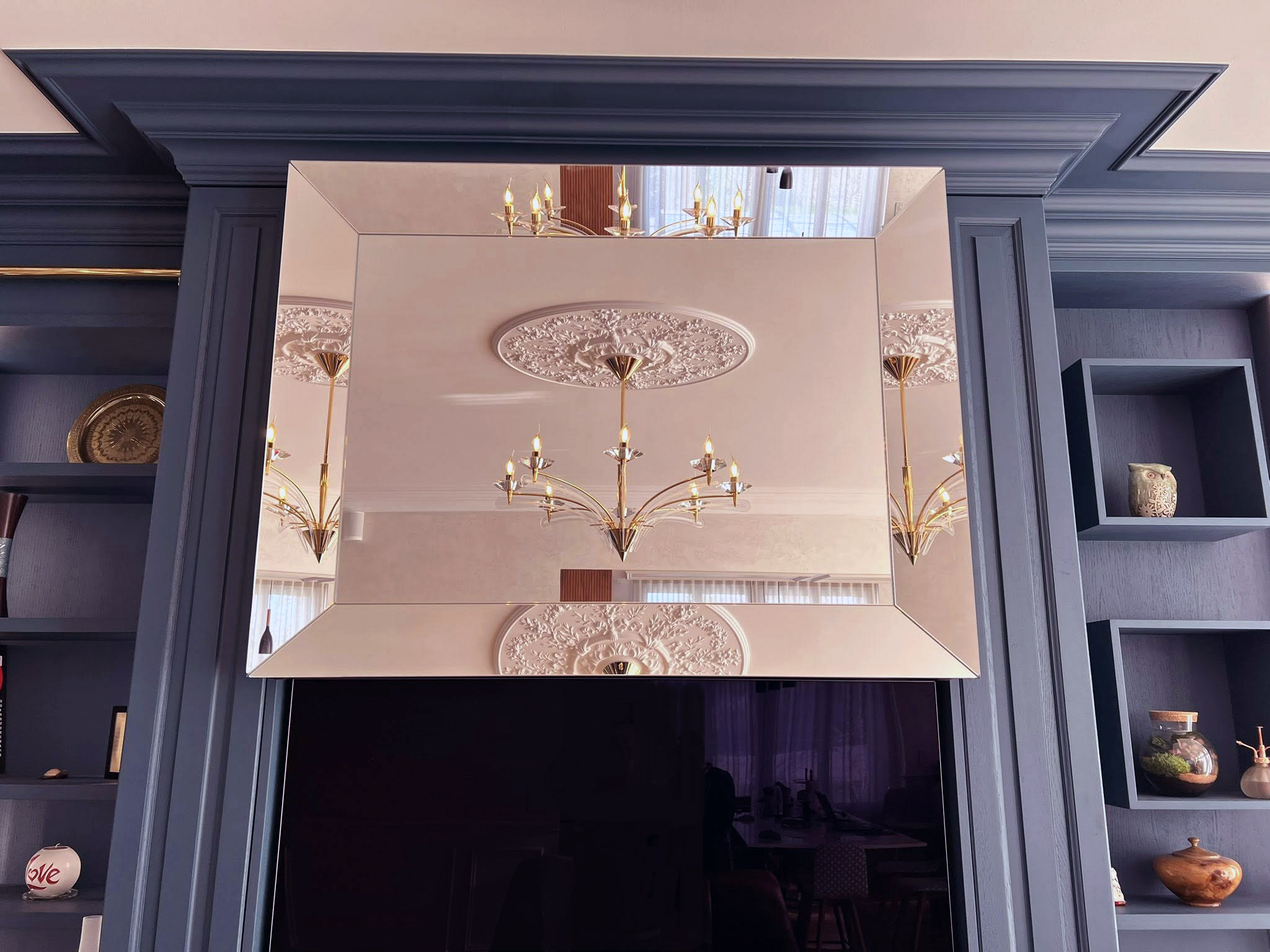 Miroir biseauté disposé sur un panneau dissimulant une télévision au-dessus de la cheminée